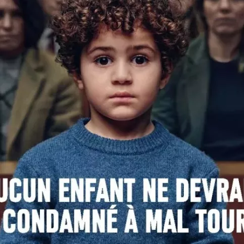 Un petit garçon d'environ 4 ans est menotté dans un tribunal. On voit derrière lui le public un peu flouté. Texte : Aucun enfant ne devrait être condamné à mal tourner. Apprentis d'Auteuil soutient chaque année 40 000 jeunes en difficulté pour qu'ils puissent se bâtir un avenir meilleur. Faites un don sur www.apprentis-auteuil.org
